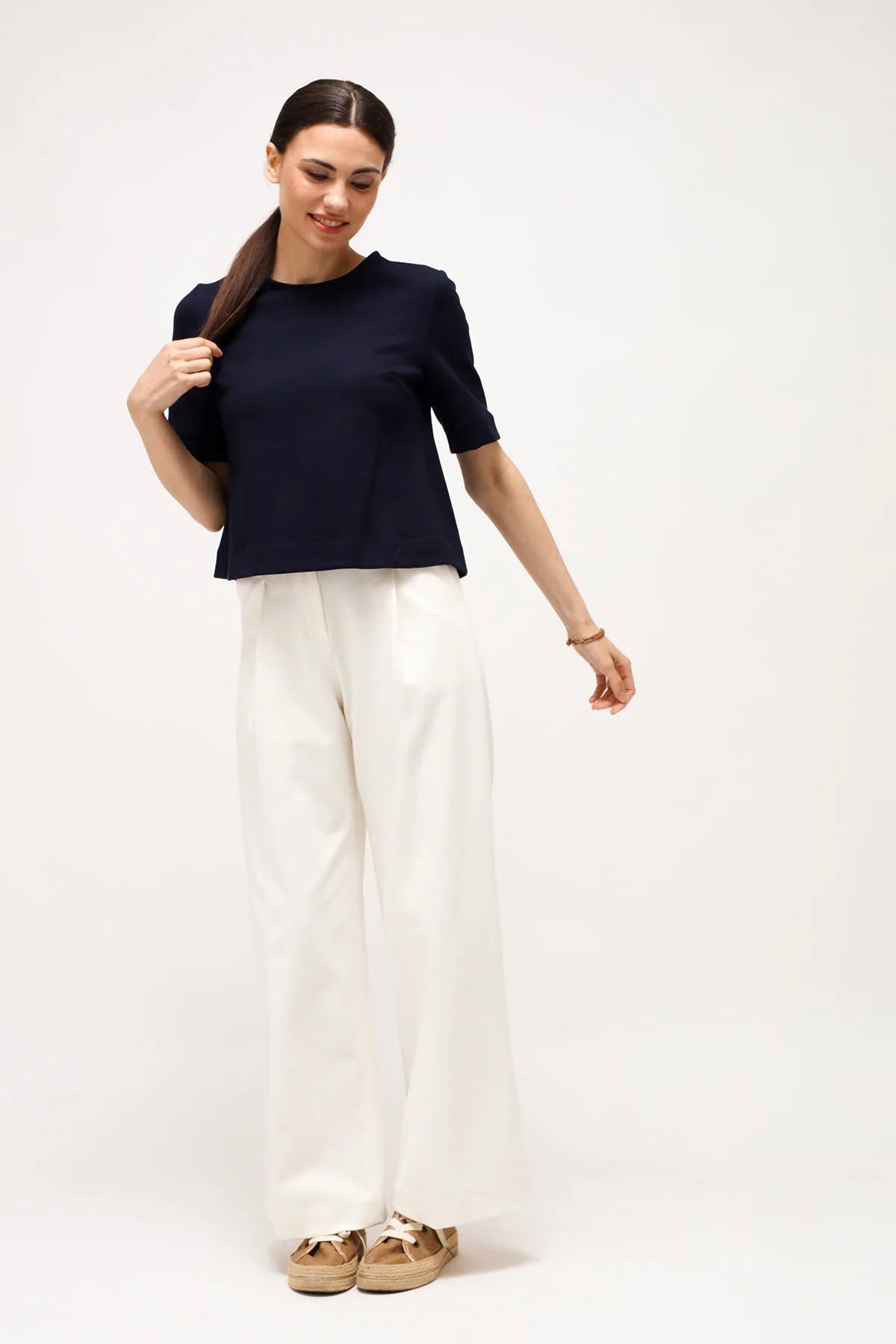 A woman wearing a Milano Stitch (Punto Milano) blue top and white palazzo pants on a white seamless background.